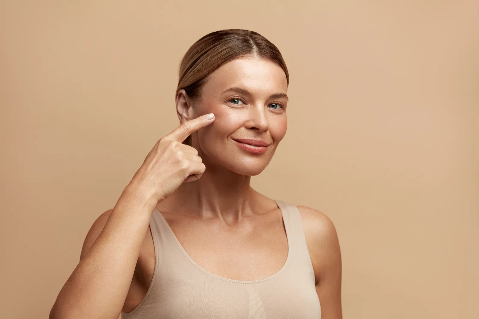 Lifting-Weilheim-Starnberg-Schongau Frau mit strahlender Haut, die auf Gesicht zeigt zur Faltenunterspritzung Behandlung der Heilpraxis Schönheilen in Weilheim bei Schongau